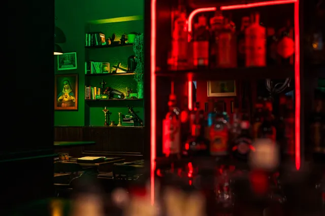 Love & Poison bar interior - red neon glow behind the bar with the green-walled nook visible through a doorway