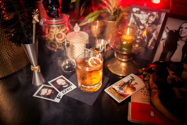 A negroni cocktail with dried orange garnish, surrounded by polaroids and tarot cards