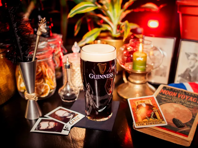 A Guinness pint on the bar surrounded by polaroids, dried citrus, and vintage books